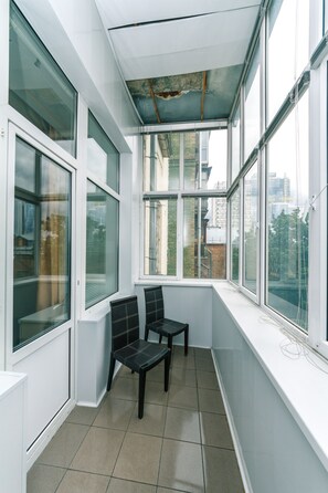 A small, enclosed balcony with two chairs, large windows, and a view of the city.
