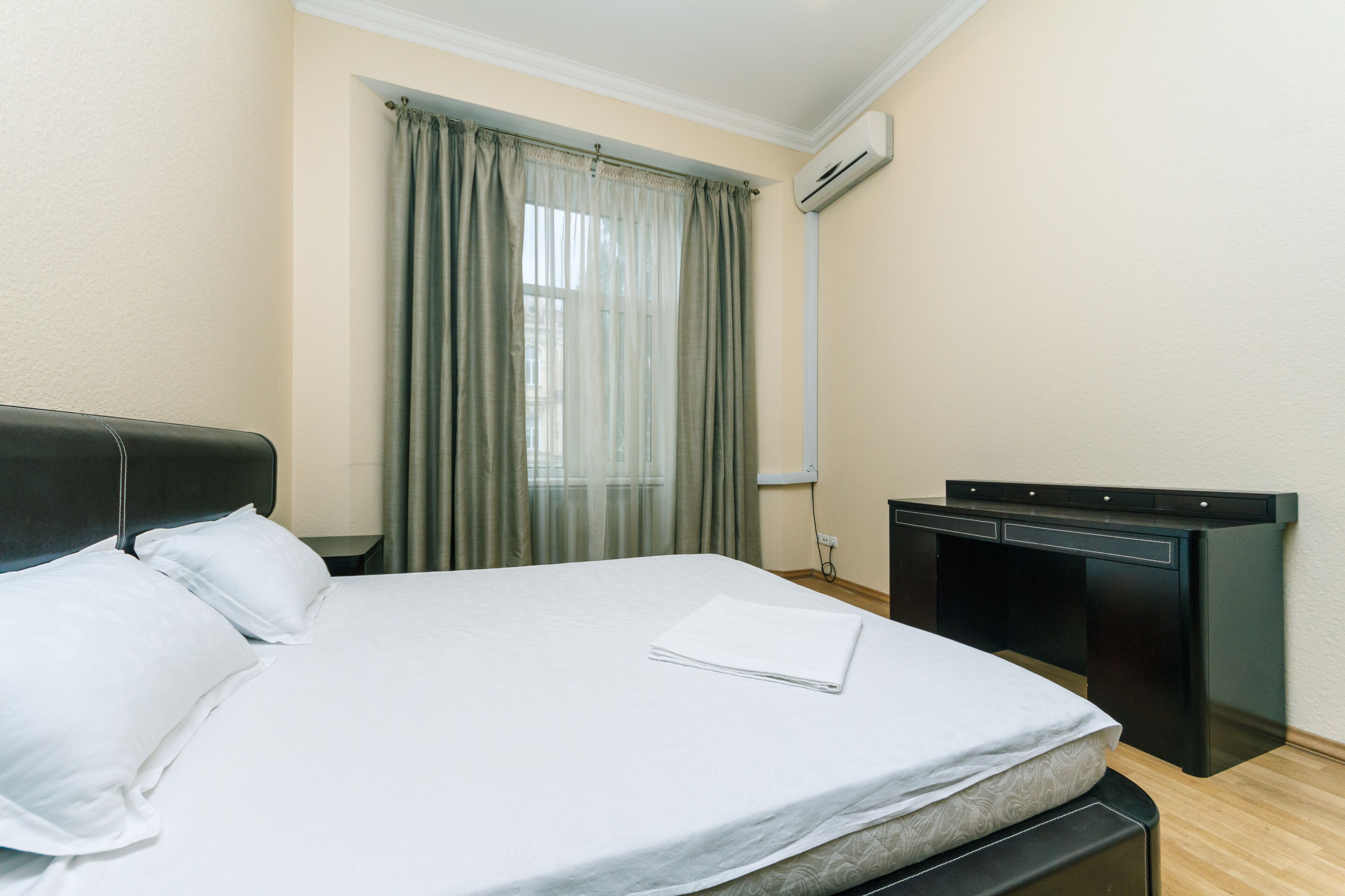 A neatly made bed with white linens, a dark headboard, and a small desk with a black finish.