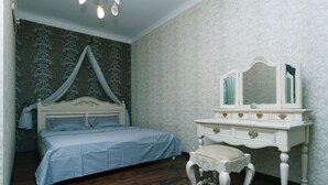 Een slaapkamer met een hemelbed, een kaptafel met spiegel en een klein krukje.