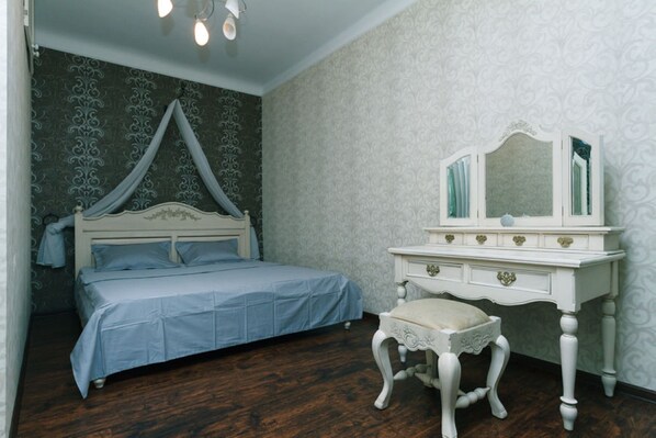 A bedroom with a four-poster bed, a vanity with a mirror, and a small stool.
