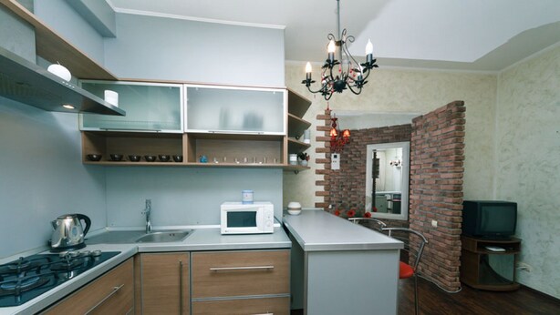 Een moderne keuken met een magnetron, fornuis en houten keukenkastjes. Er is een bakstenen muur en een televisie in de hoek.
