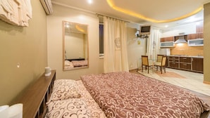 A bedroom with a large bed, a desk, and a kitchenette.