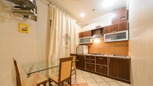 A compact kitchen with wooden cabinets, a microwave, and a gas stove. There is a glass dining table with chairs.