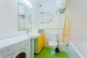 Une petite salle de bain équipée d’un lave-linge, d’un évier, de toilettes et d’une baignoire.