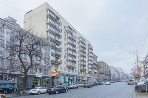 Un immeuble à plusieurs étages doté de balcons, une rue pavée et des voitures garées.