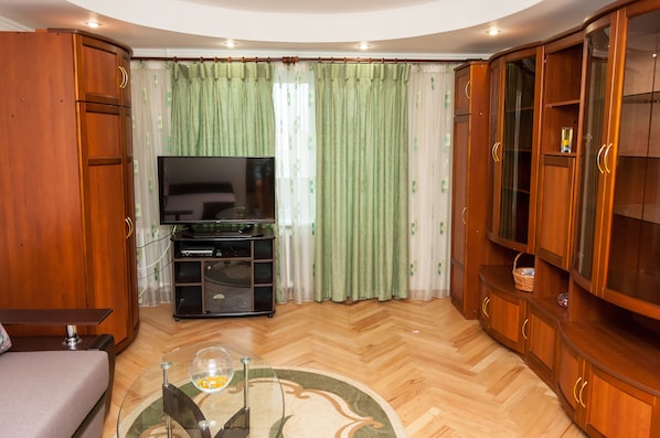 A living room with a flat-screen TV, wooden cabinets, a sofa, and a glass coffee table.