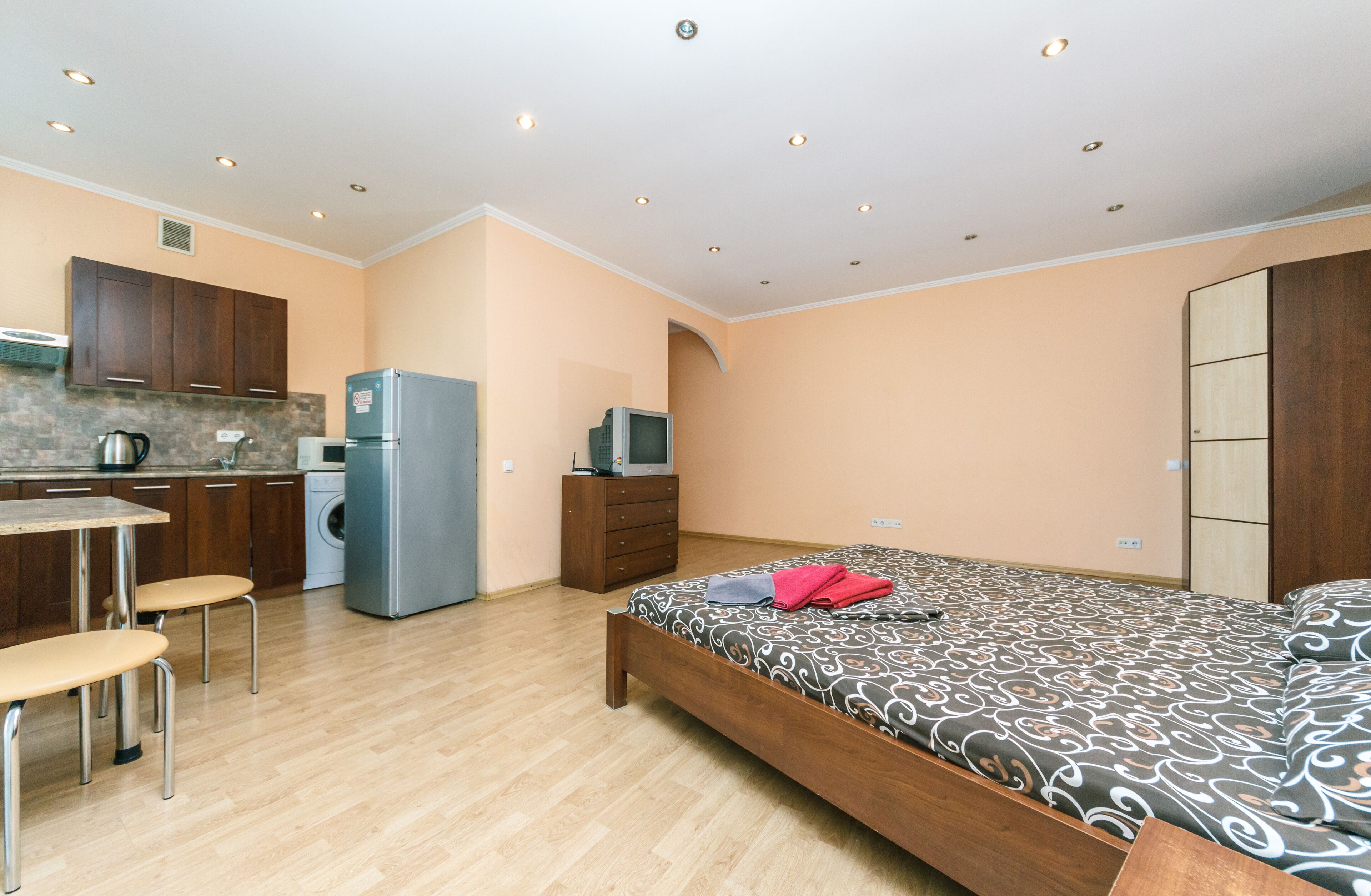 Quarto compacto com cama, pequena cozinha e área de refeições.