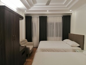 A modern hotel room with two beds, a wardrobe, a small seating area, and a large window with curtains. - Roma Hotel Noi Bai airport (Hanoi)