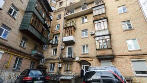 Un edificio de apartamentos de varios pisos con balcones, un coche aparcado y suelo cubierto de nieve.