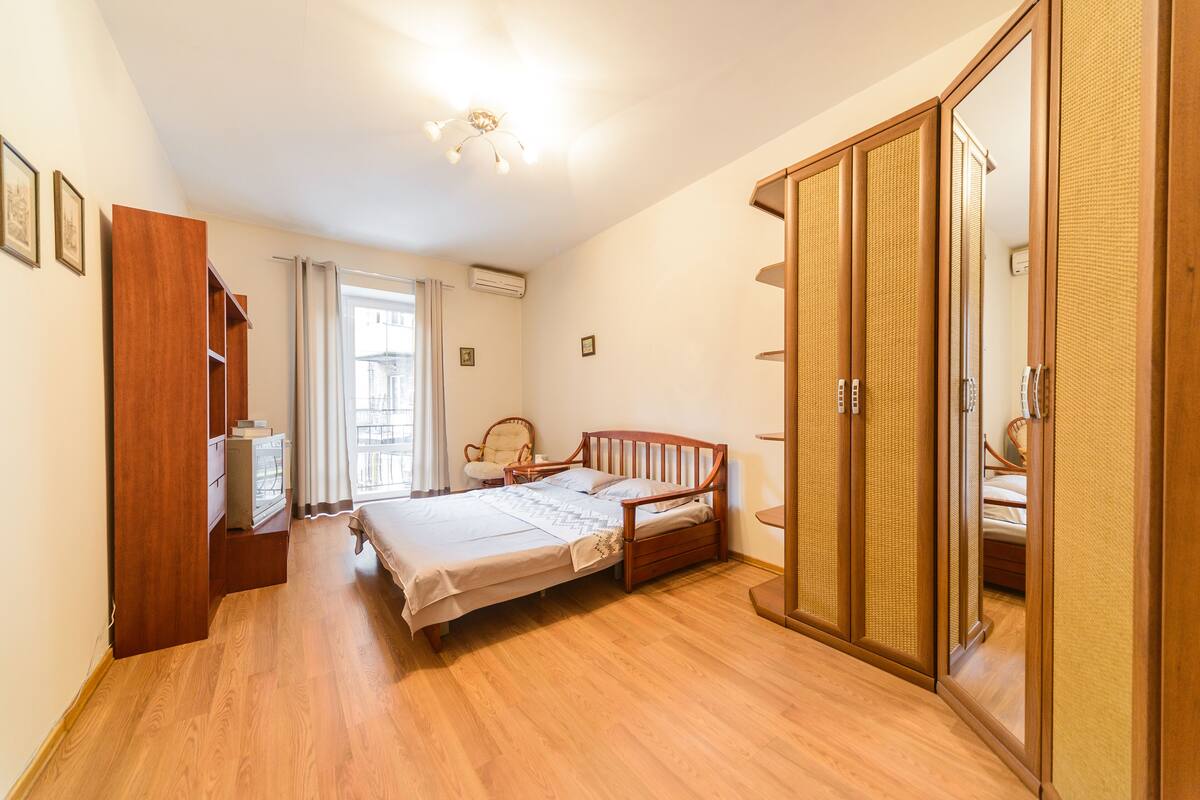 A bedroom with a wooden bed, a wardrobe, a chair, and a desk with a lamp.