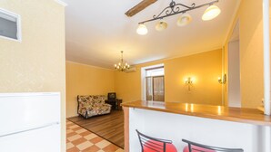 A compact kitchen with a wooden countertop, two red bar stools, a patterned sofa, and a chandelier. - Cozy studio apartment near Palace Ukraina (Kyiv)