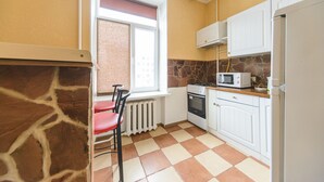 A kitchen with white cabinets, a stove, a microwave, and a window with a curtain. - Cozy studio apartment near Palace Ukraina (Kyiv)