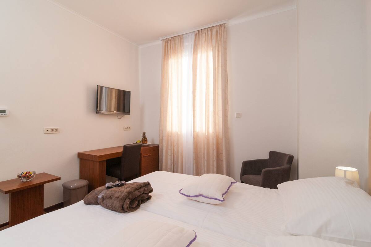 A hotel room with a bed, a desk, a chair, a TV, and a window with curtains.