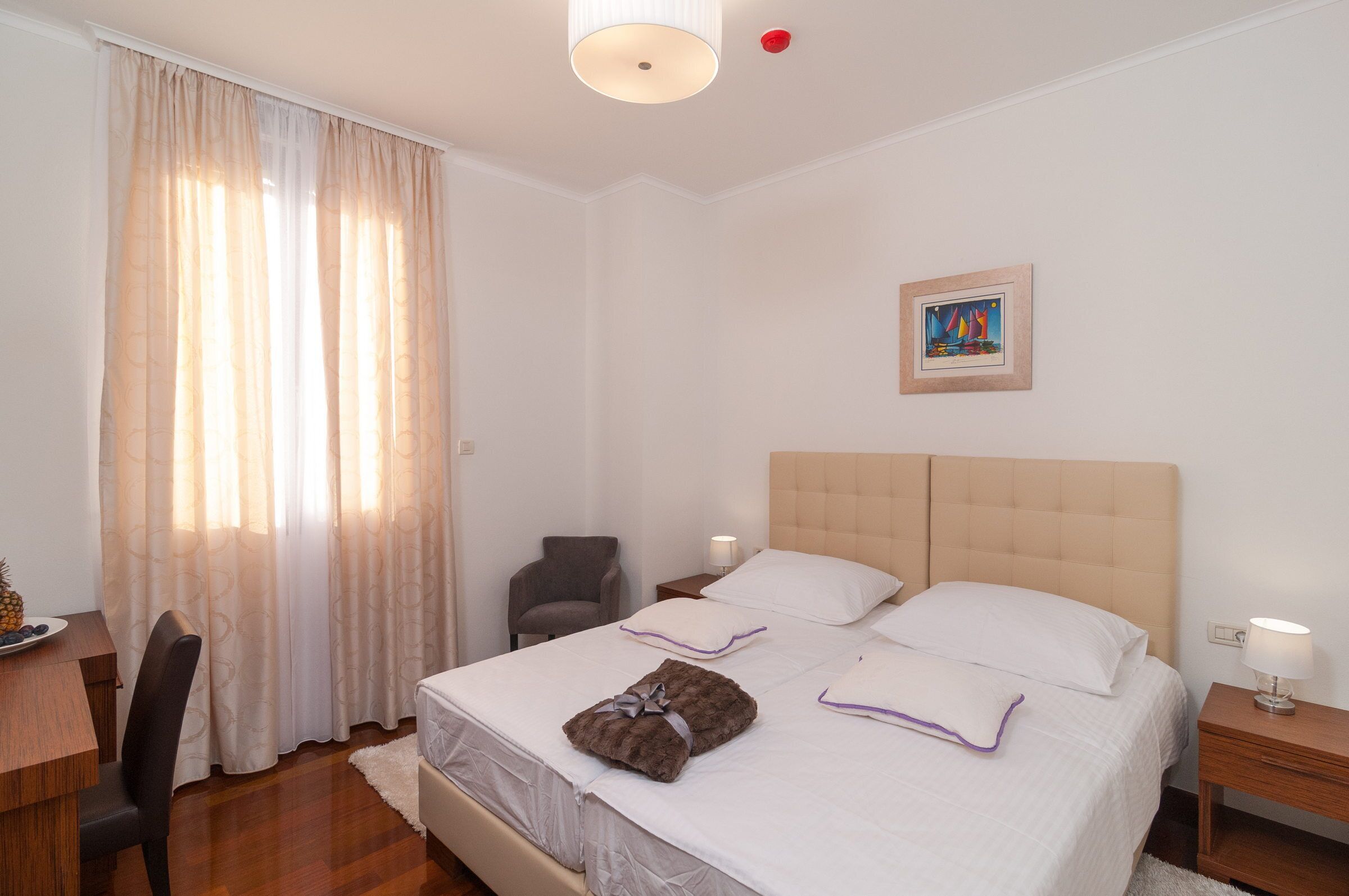 A hotel room with a bed, a desk, a chair, and a painting on the wall.