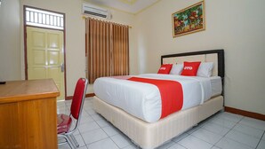 Une chambre d’hôtel comprenant un lit, un bureau, une chaise, un appareil de climatisation, une porte et une fenêtre avec des rideaux.