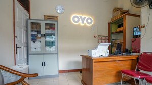 Un espace d’accueil avec un bureau en bois, une chaise rouge, une vitrine contenant du matériel de bureau et une horloge au mur.