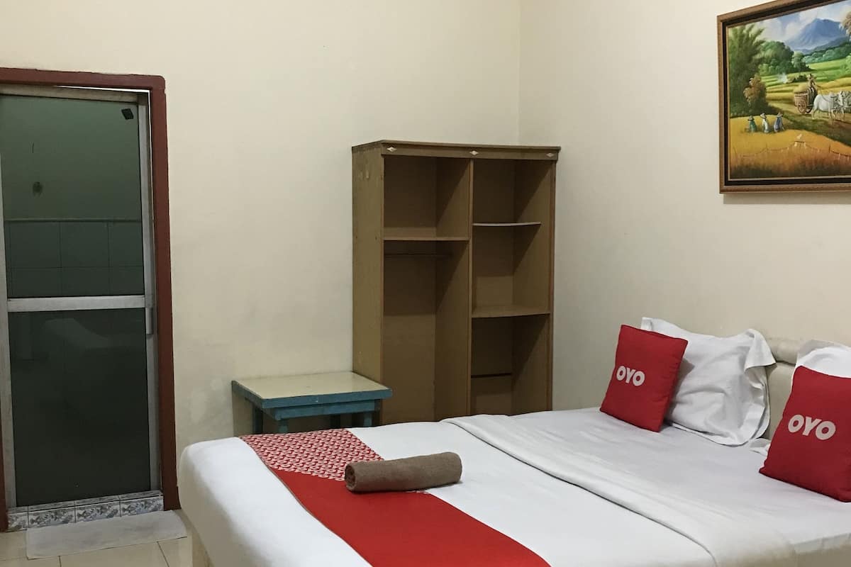 Een hotelkamer met een bed, een klein tafeltje, een kledingkast en een schilderij aan de muur.