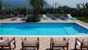 A rectangular swimming pool with a tiled edge, surrounded by lounge chairs and a pergola with lights.