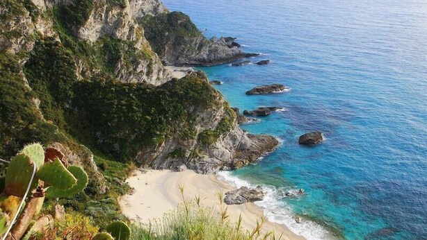 A coastal landscape with a sandy beach, rocky cliffs, and clear blue waters.