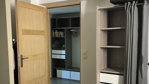 Una habitación con puerta de madera, un armario con estantes y una cortina gris.