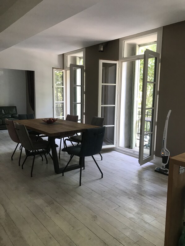 Un espace repas avec une table et des chaises en bois, de grandes fenêtres et une vue sur l’extérieur.