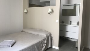 Un dormitorio con una cama, una mesita de noche, un espejo y un baño con lavamanos y espejo.