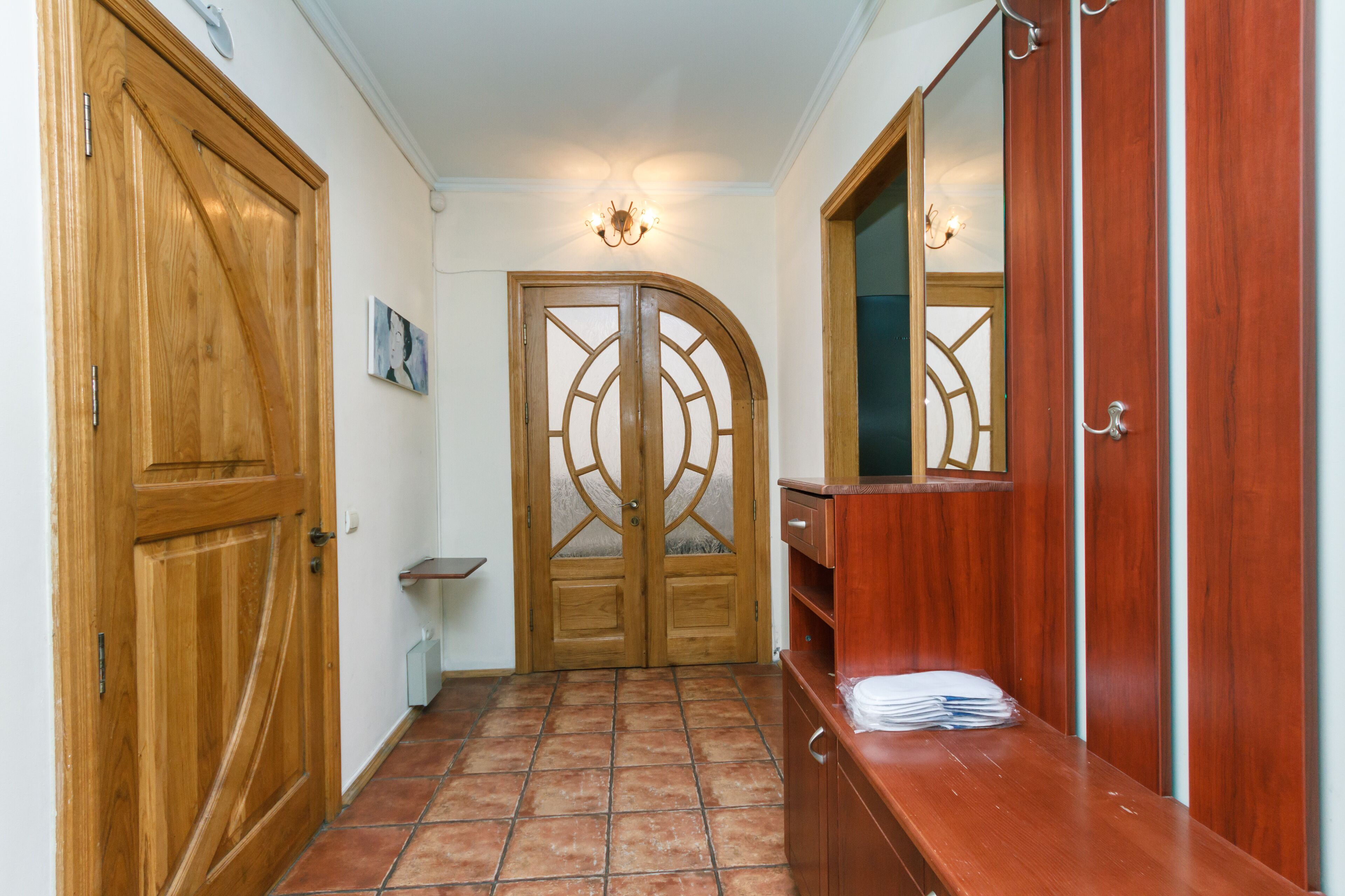 A hallway with wooden doors, a tiled floor, a mirror, and a bench with folded towels.