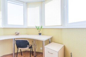 Une pièce d’angle avec un bureau blanc, une chaise noire, une petite plante en pot et un classeur blanc.
