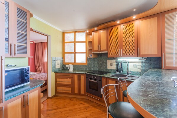 A compact kitchen with wooden cabinets, a microwave, a stove, and a sink. - Obolon apartment 73 (Kyiv)