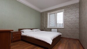 A bedroom with a wooden bed, a nightstand, a dresser, and a window with blinds. - Apartment on Obolon (Kyiv)