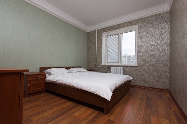 A bedroom with a wooden bed, a nightstand, a dresser, and a window with blinds.