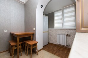 A compact kitchen with a wooden table and chairs, a refrigerator, and a window with blinds.