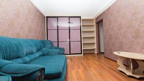 A room with a teal sofa, wooden flooring, a sliding door closet, and a small table. - Apartment on Obolon (Kyiv)