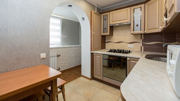 A compact kitchen with a wooden table, built-in cabinets, a stove, and a sink. - Apartment on Obolon (Kyiv)