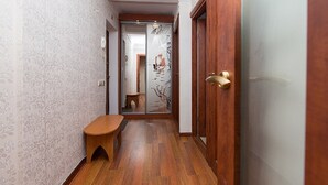 A narrow hallway with patterned wallpaper, a wooden bench, and a door with a brass handle. - Apartment on Obolon (Kyiv)