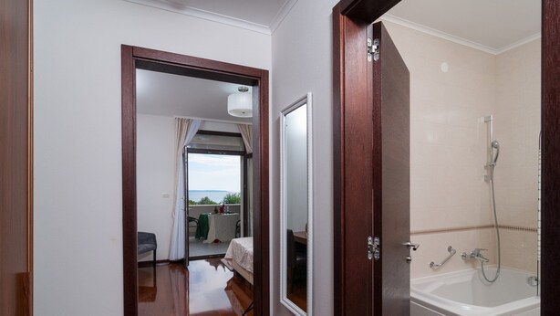 Habitación de hotel con piso de madera, una bañera blanca y un balcón con mesa y sillas.