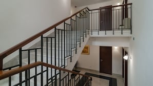 Un interior con varios niveles, una escalera de madera, barandillas negras y una puerta.