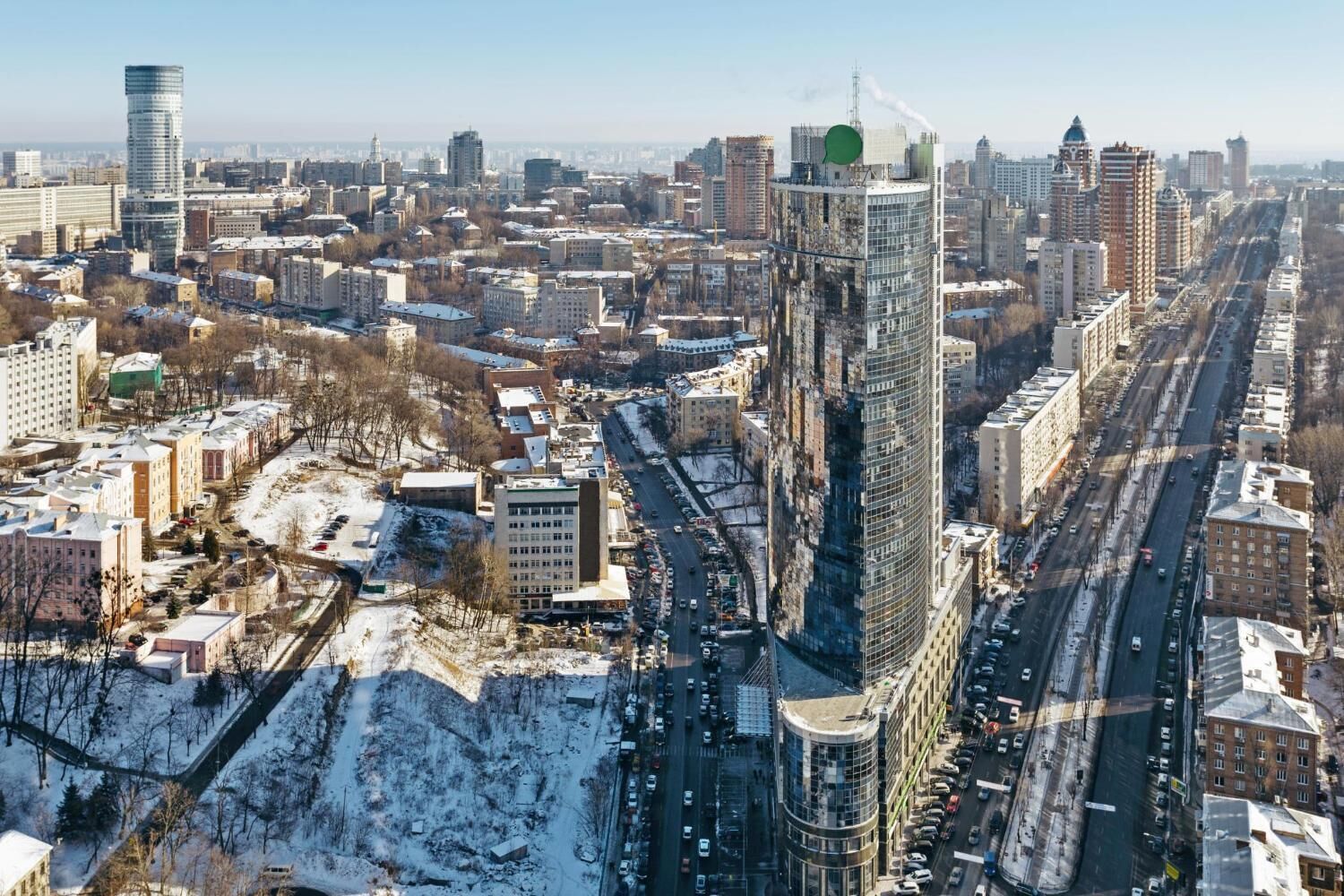 Un paisaje urbano con un rascacielos curvo destacado, varios edificios y una zona nevada al frente.