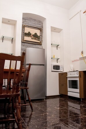 A kitchen with a refrigerator, microwave, stove, and wooden chairs. - Apartment near Arena City (Kyiv)