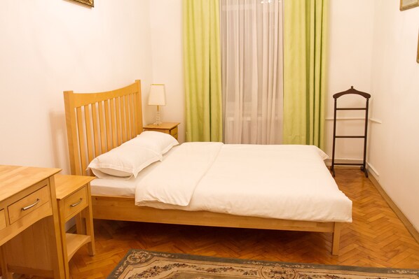 A neatly made bed with a wooden headboard, a bedside table with a lamp, and a hanging rack.