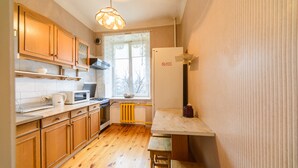 A compact kitchen with wooden cabinets, a microwave, a kettle, and a window with a view of bare trees. - Apartment near Olympic Stadium (Kyiv)