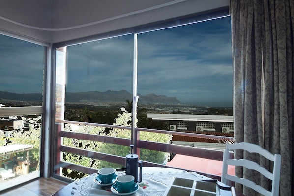 Un balcón con mesa y sillas, con vistas a un paisaje urbano y montañas.