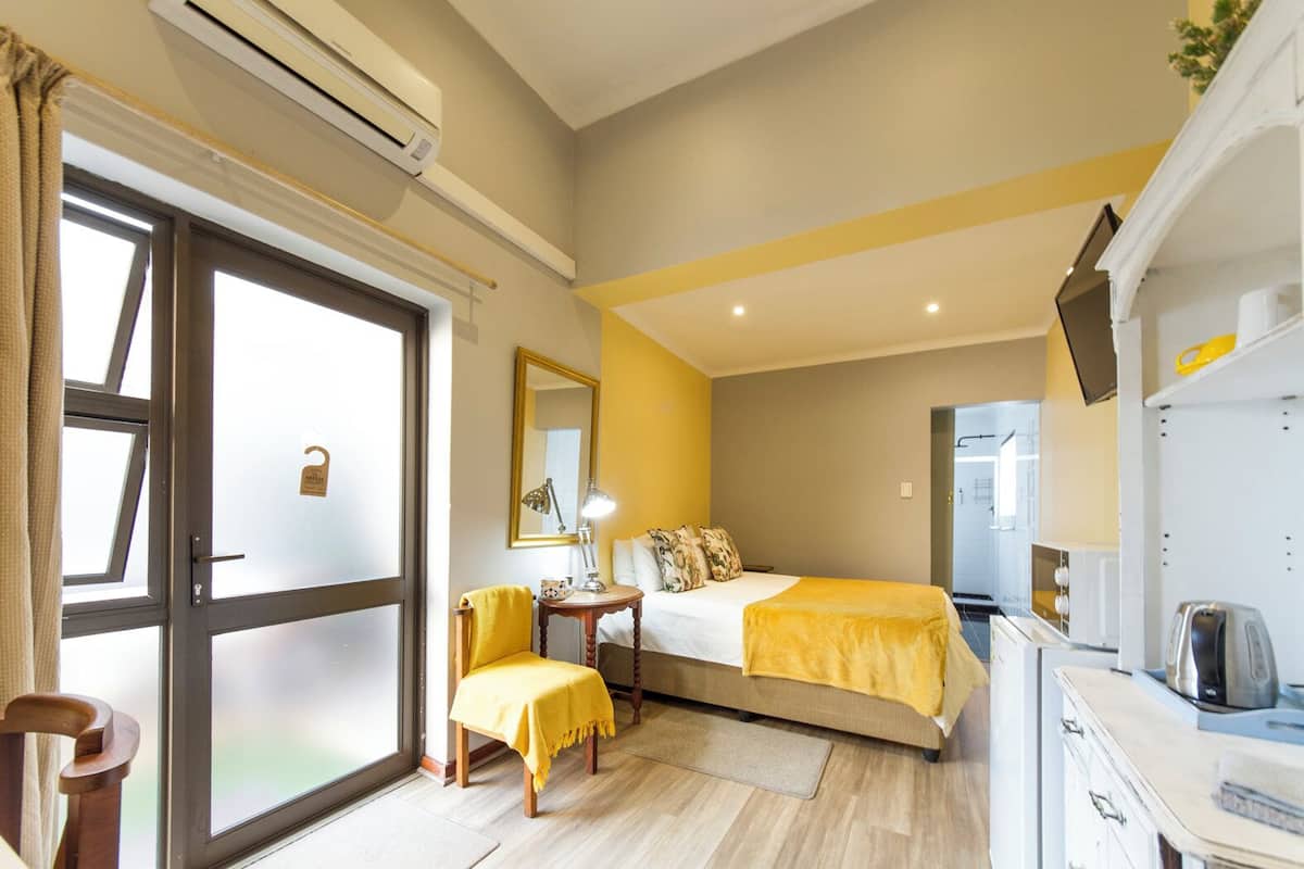 A hotel room with a bed, a desk, a chair, a mirror, and a sliding glass door.