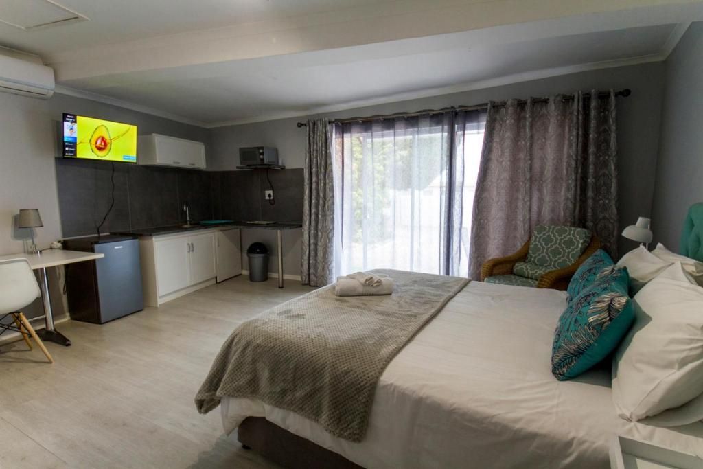 A bedroom with a bed, a desk, a kitchenette, and a TV on the wall.