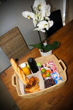 A wicker basket with food items, a bottle, and a plant on a wooden table. - Bed & Breakfast Crosne Plazza & Spa (Crosne)