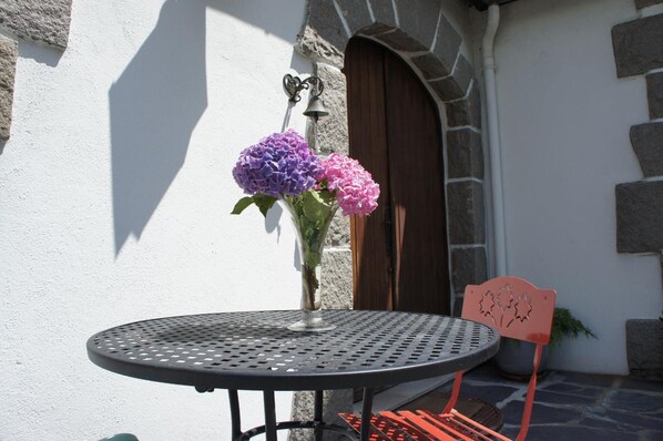 A round metal table with a clear glass vase containing purple and pink flowers, positioned in front of a stone wall with a wooden door. - Bed & Breakfast Crosne Plazza & Spa (Crosne)
