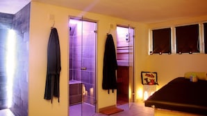 Una habitación con una cama, una mesita con una vela y una puerta que da a un baño con iluminación morada.