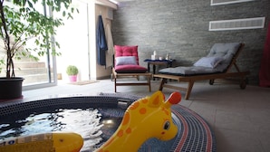 Una habitación con piscina, un flotador con forma de jirafa, una silla, una mesa y una planta en maceta.
