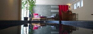 Una habitación con una amplia piscina reflectante, una silla roja, un armario de madera y una planta en maceta.