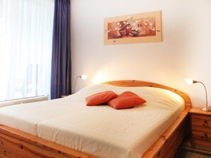 Una cama bien tendida con cabecera de madera, un cuadro en la pared y una ventana con cortinas.